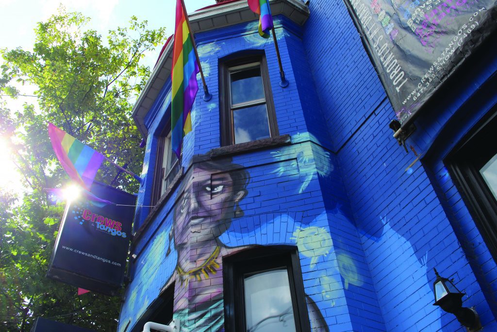 Blue brick building with painting of woman and rainbow flags hanging