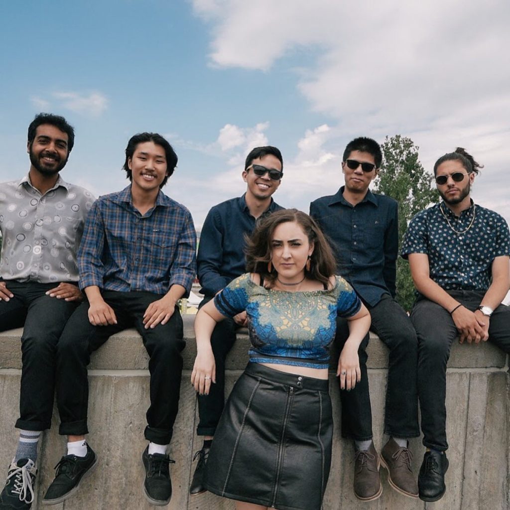 a woman in a blue shirt stands in front of four men sitting on a concrete slab