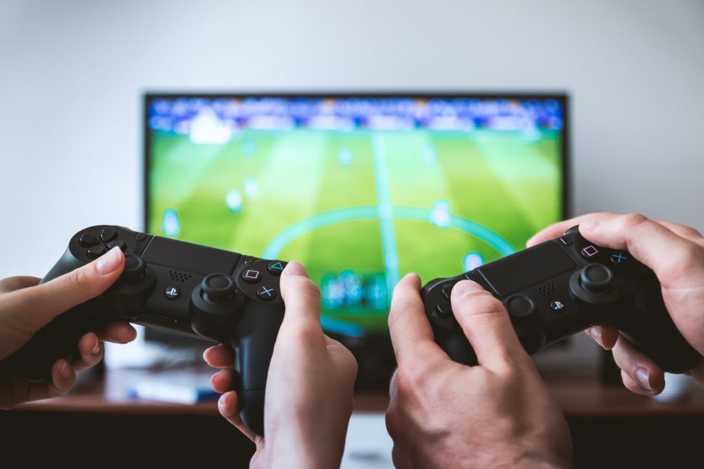 two hands with controllers playing a soccer video game on a television set in front of them