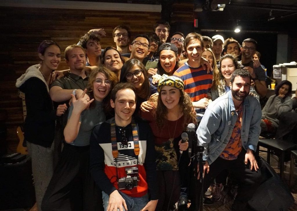 A group of students stand huddled together smiling for the camera with mics in hand