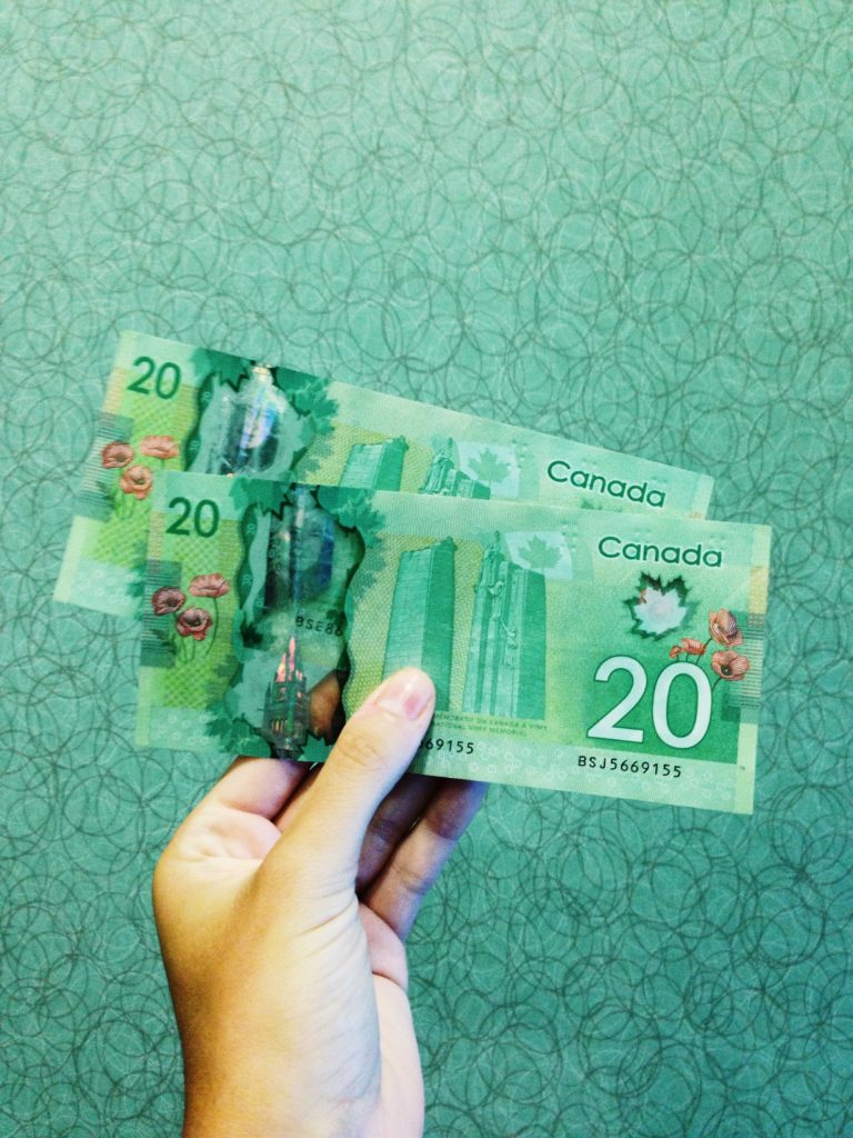 a white hand holds a pair of 20 dollar Canadian bills