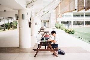 A student sits alone at a picnic table outside, using his laptop.