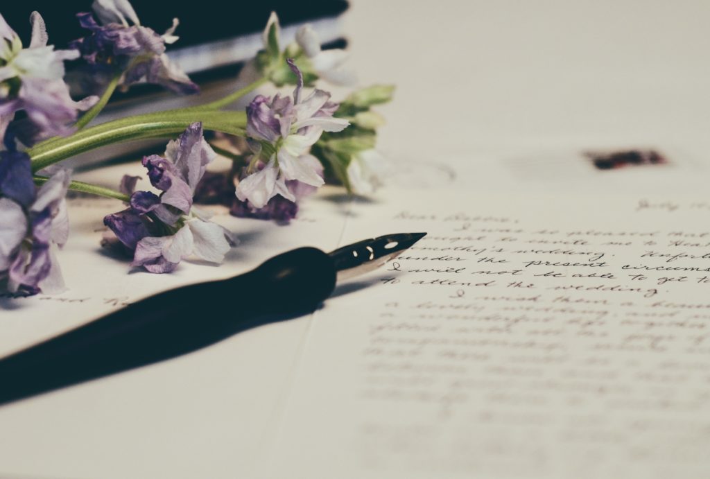 a pen is on a paper with words on it with purple lillies on the left handside