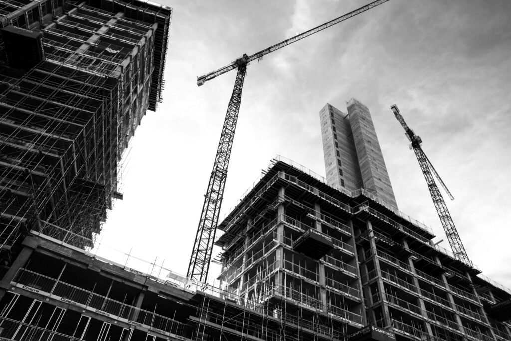 A black and white image of buildings under construction and a large crane in the sky