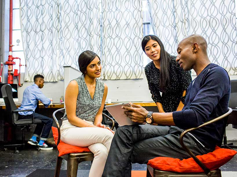 three people sit on red chairs in a circle listening intently to one another