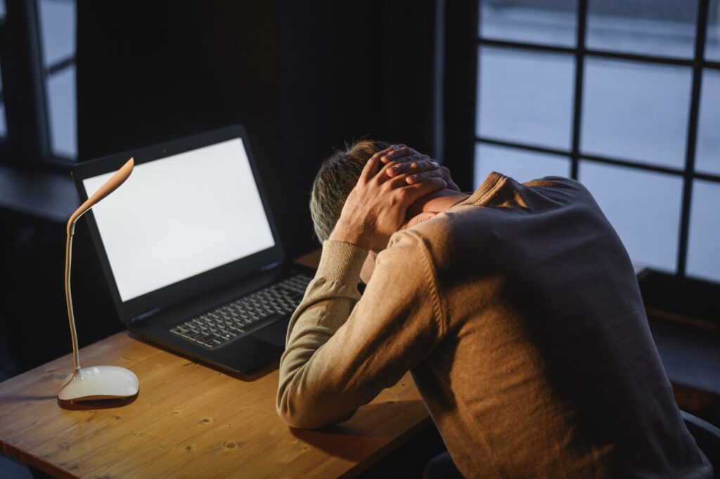 a man sits at a desk in front of his computer with his head in his hands