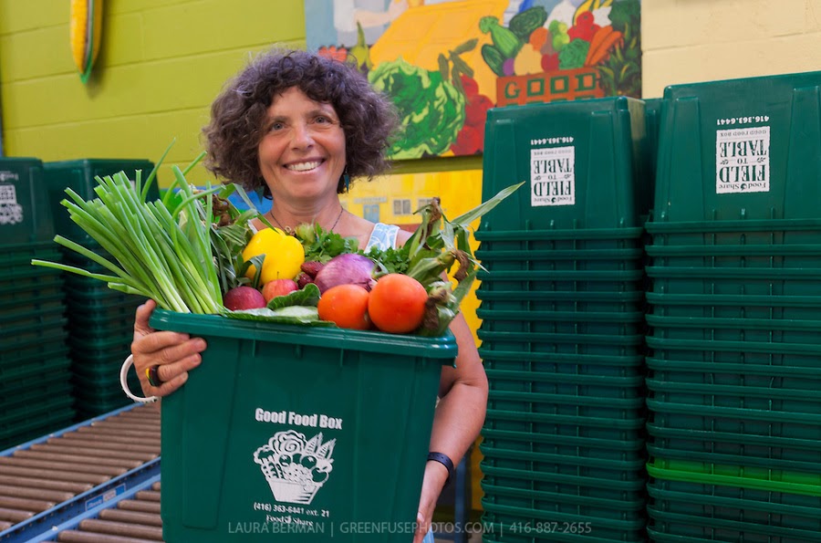 a woman holds a green box filled to the brim with vegetables and other produce